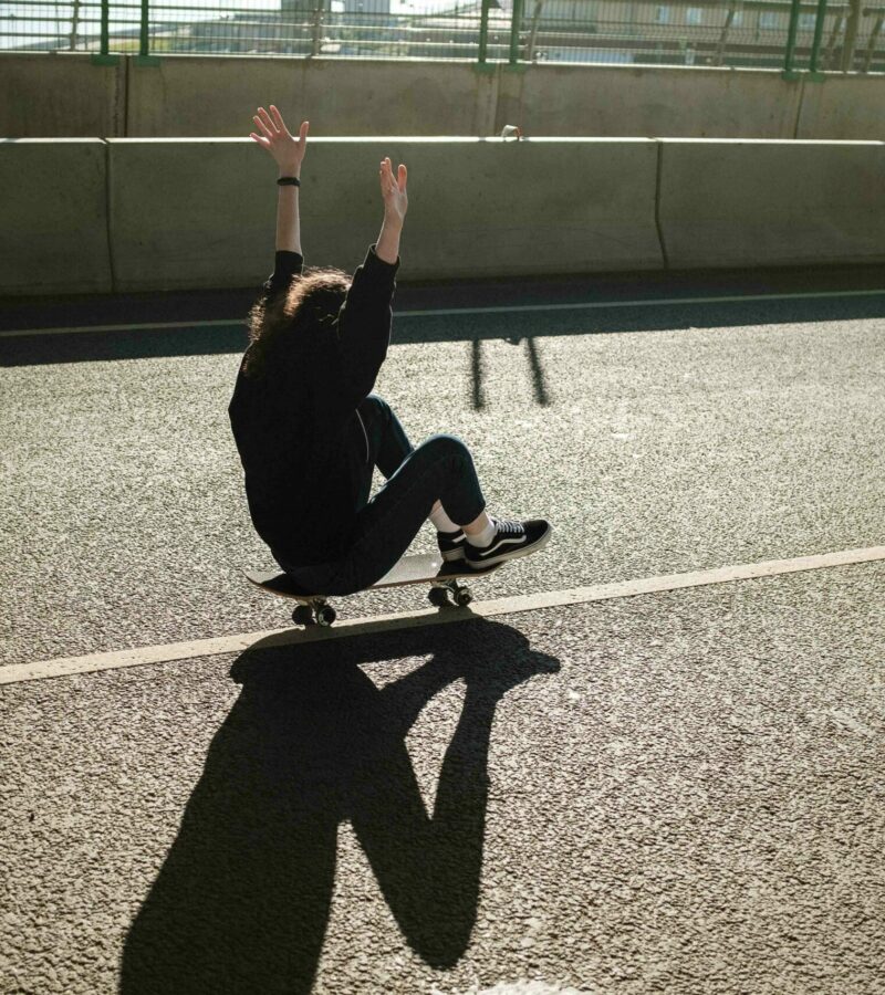 Frau sitzt jubelnd auf einem Skateboard und fährt über den Highway