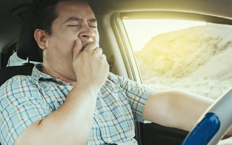 View of a sleepy driver in his car. Tired driver yawning in the car, concept of man yawning while driving. A sleepy driver at the wheel, a tired person while driving